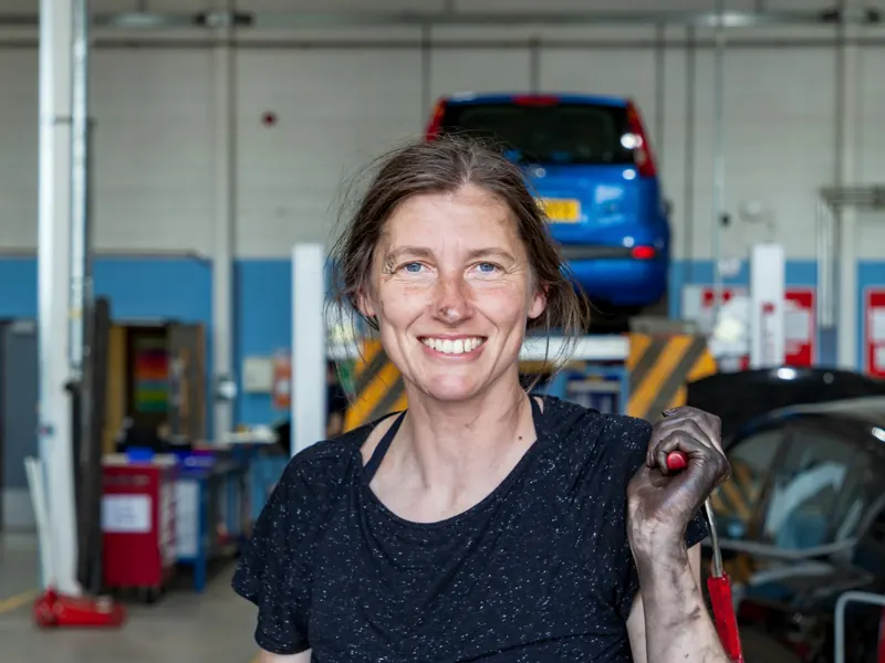 Smiling mechanic holding a tool in her auto shop