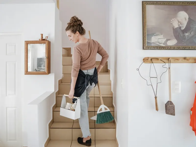 Cleaner carrying supplies and a broom up the stairs of a home