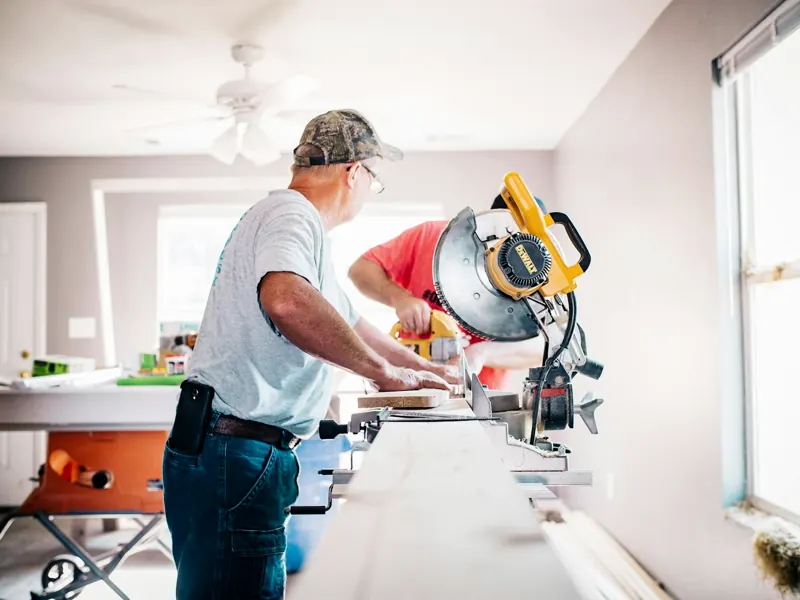 Handyman cutting wood with a miter saw inside a home