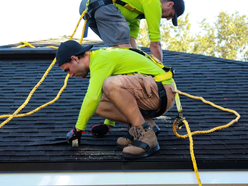 Two roofers working on a house roof with safety harnesses